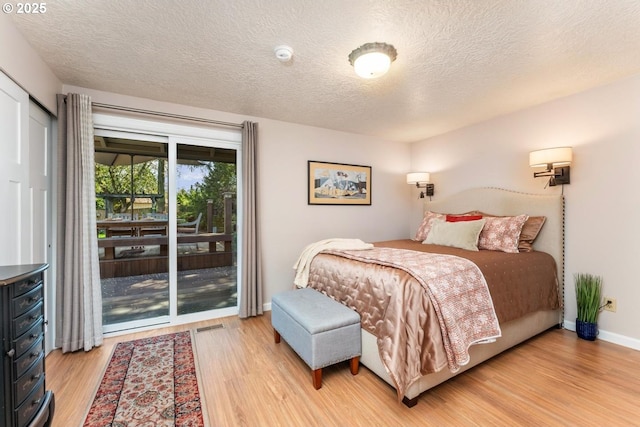 bedroom featuring baseboards, light wood finished floors, a textured ceiling, and access to exterior