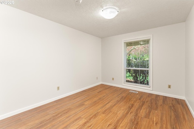unfurnished room featuring light wood-style floors, a textured ceiling, baseboards, and visible vents
