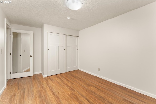 unfurnished bedroom featuring baseboards, a closet, light wood-type flooring, and a textured ceiling