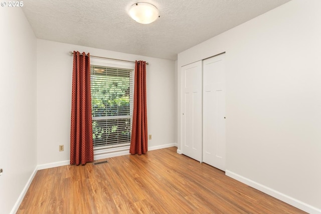 unfurnished bedroom with visible vents, a closet, baseboards, a textured ceiling, and light wood-style flooring