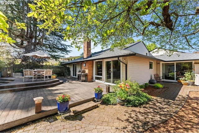 rear view of house with outdoor dining area, fence, a chimney, and a deck
