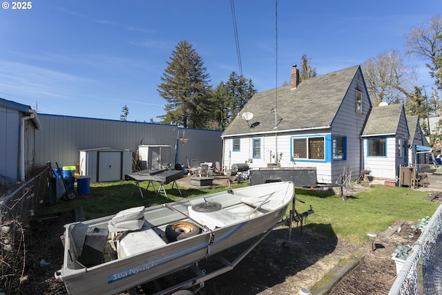 back of property featuring an outbuilding, a chimney, a storage unit, a lawn, and an outdoor fire pit