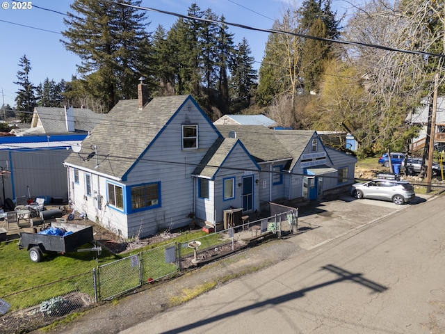 view of front facade with a shingled roof, a fenced front yard, and a chimney