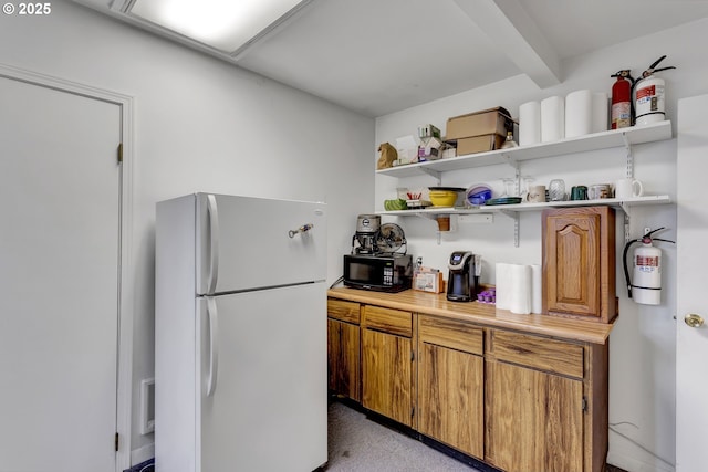 kitchen with black microwave, light countertops, freestanding refrigerator, open shelves, and brown cabinetry