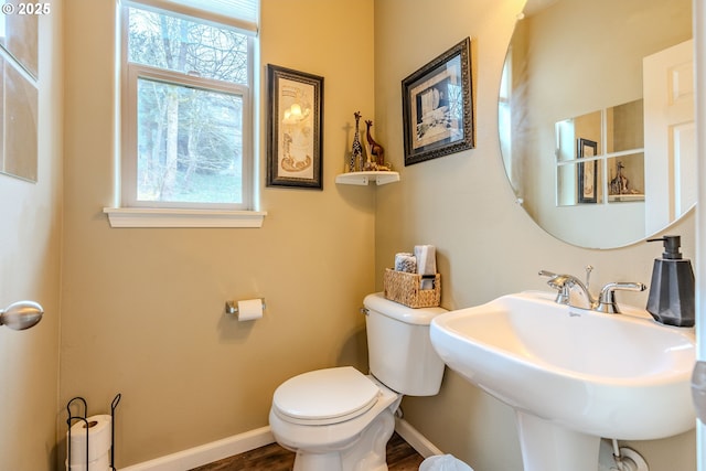 half bath featuring toilet, baseboards, a sink, and wood finished floors