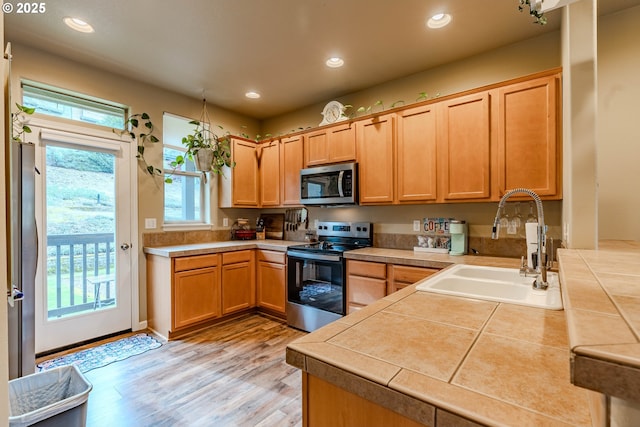 kitchen with tile counters, light wood-style flooring, appliances with stainless steel finishes, a sink, and recessed lighting