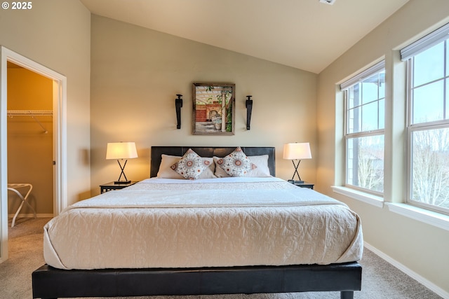 carpeted bedroom with vaulted ceiling, a walk in closet, and baseboards