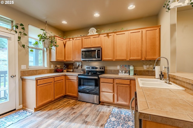 kitchen with tile countertops, stainless steel appliances, recessed lighting, a sink, and light wood-type flooring