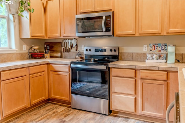 kitchen with tile countertops, light wood finished floors, light brown cabinets, and stainless steel appliances