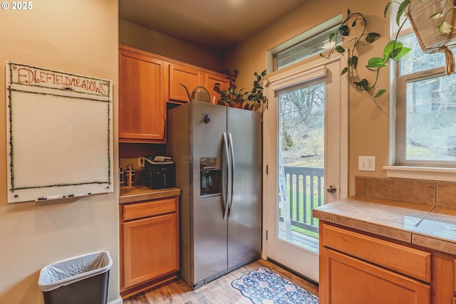 kitchen featuring tile counters, brown cabinetry, stainless steel fridge, and light wood-style flooring