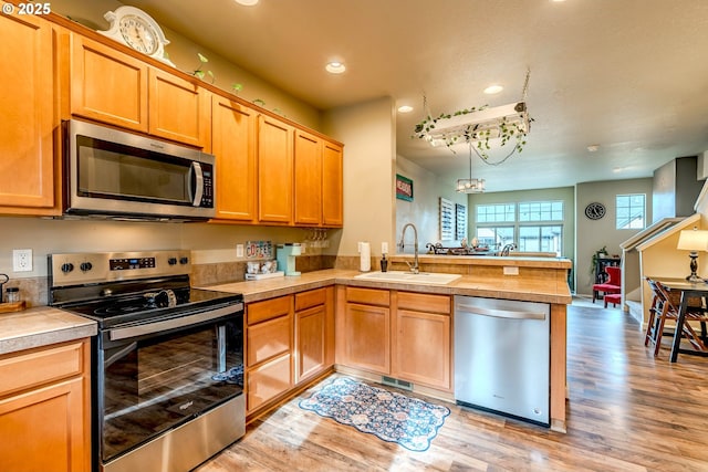 kitchen with light wood finished floors, a peninsula, appliances with stainless steel finishes, and a sink