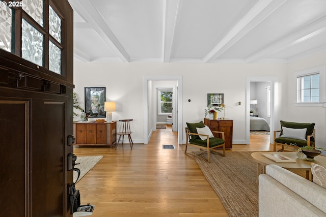 foyer entrance featuring beamed ceiling, plenty of natural light, light wood-style floors, and baseboards