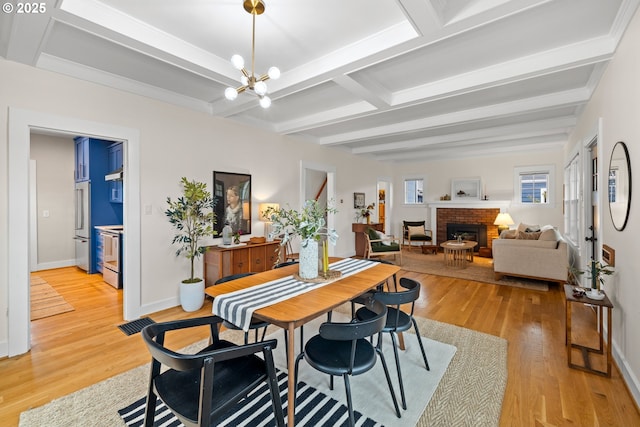 dining area with light wood-style flooring, a fireplace, beamed ceiling, baseboards, and a chandelier