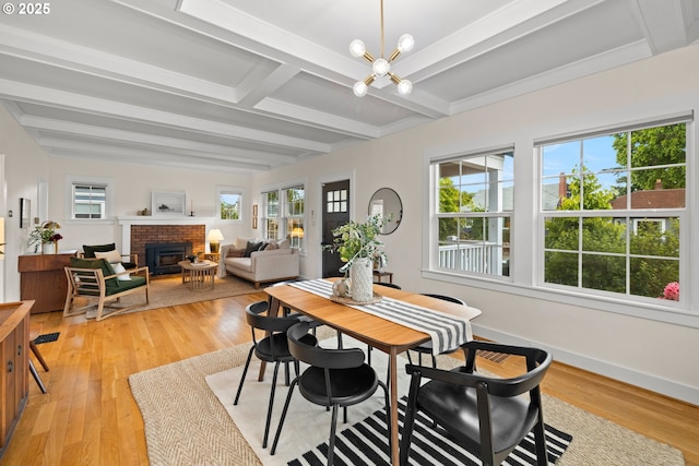 dining area featuring beamed ceiling, a chandelier, light wood finished floors, a brick fireplace, and baseboards
