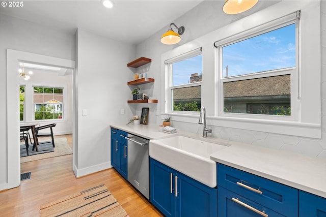 kitchen with blue cabinets, stainless steel dishwasher, a sink, light wood finished floors, and light countertops