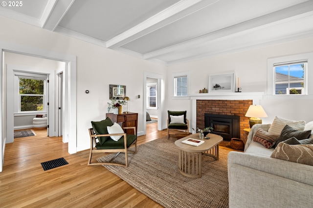 living room with beamed ceiling, plenty of natural light, light wood-type flooring, and a brick fireplace
