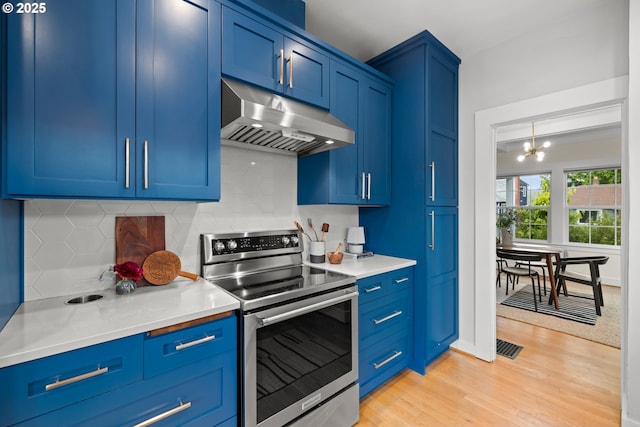 kitchen featuring stainless steel range with electric stovetop, under cabinet range hood, blue cabinetry, a chandelier, and light wood-style flooring