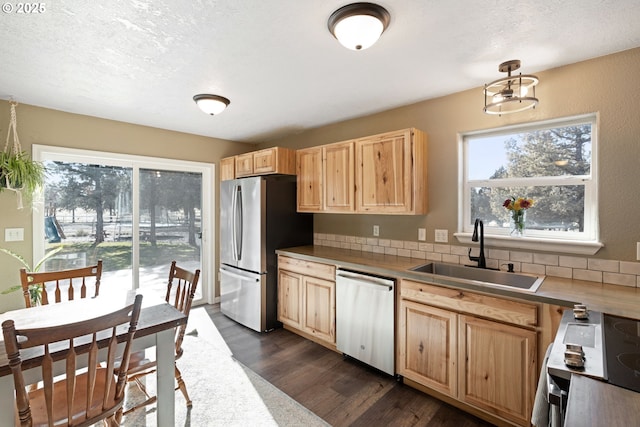 kitchen featuring a textured ceiling, light brown cabinets, stainless steel appliances, a sink, and dark wood finished floors