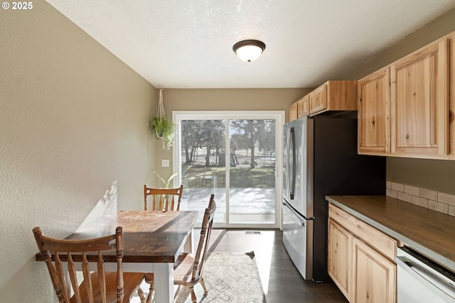 kitchen with a textured wall, light brown cabinetry, freestanding refrigerator, and dishwasher