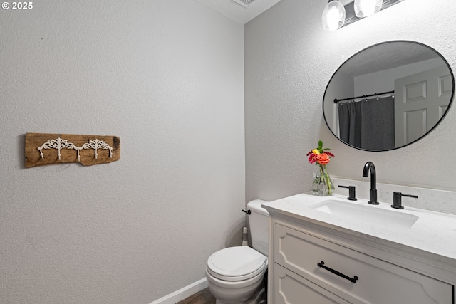 full bath featuring toilet, a textured wall, vanity, and baseboards