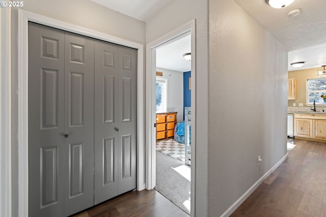 hallway with a sink, baseboards, dark wood-type flooring, and a textured wall