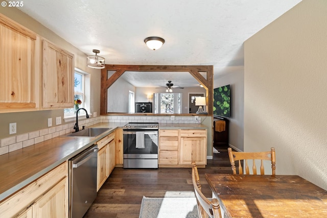 kitchen with dark wood-style flooring, stainless steel appliances, light brown cabinetry, a sink, and a peninsula