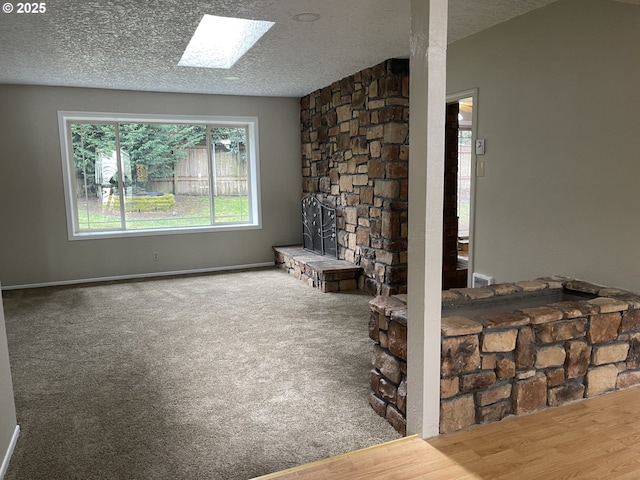 carpeted living room featuring a skylight, a textured ceiling, and baseboards