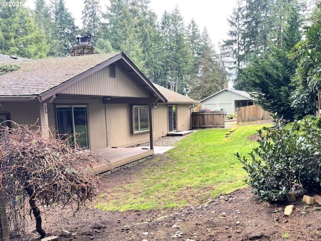 back of house featuring a shingled roof, fence, a chimney, and a lawn