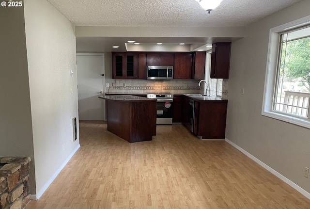 kitchen with a center island, backsplash, appliances with stainless steel finishes, light wood-style floors, and a sink