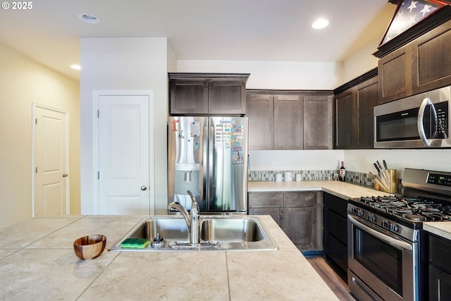 kitchen featuring dark brown cabinetry, recessed lighting, light countertops, a sink, and appliances with stainless steel finishes