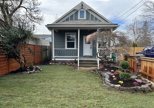 view of front of house featuring a porch, a shingled roof, a front yard, and fence