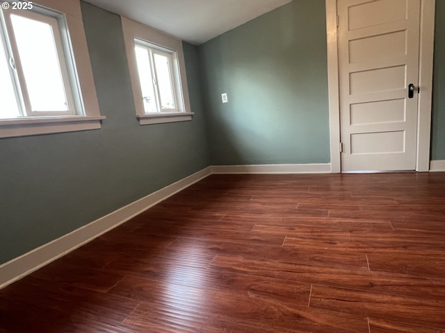 spare room featuring lofted ceiling, baseboards, and dark wood-style flooring