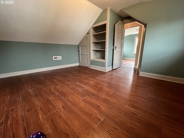 bonus room with lofted ceiling, built in shelves, visible vents, baseboards, and dark wood finished floors