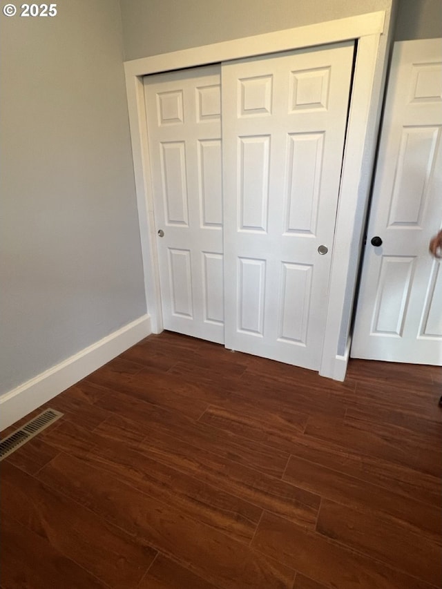 unfurnished bedroom featuring dark wood-style flooring, a closet, visible vents, and baseboards