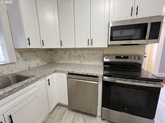 kitchen featuring white cabinets, light stone counters, backsplash, stainless steel appliances, and a sink