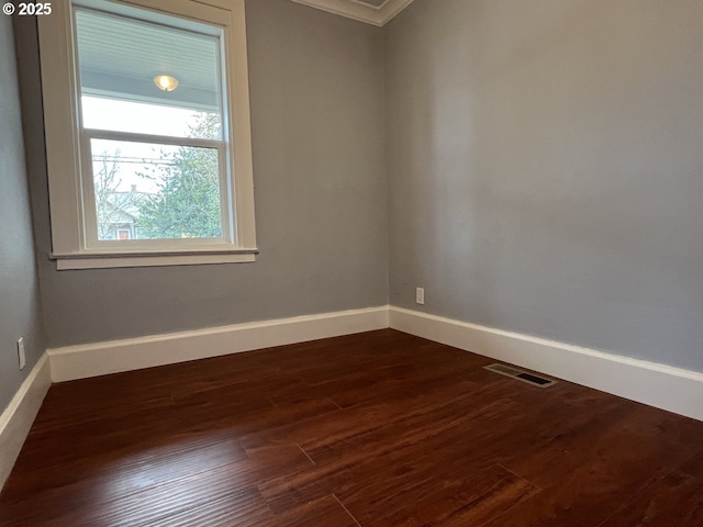 spare room with crown molding, baseboards, dark wood-style floors, and visible vents
