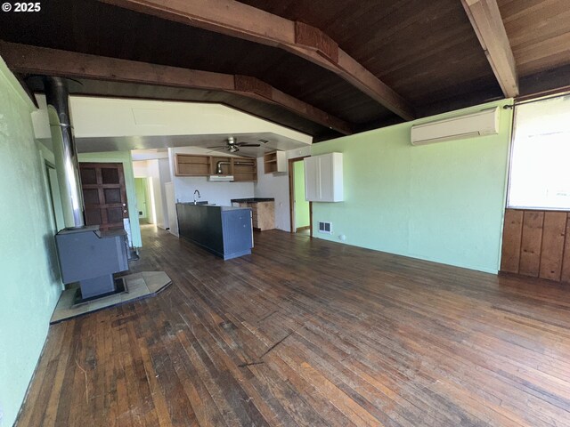 unfurnished living room with visible vents, a wall mounted AC, a wood stove, vaulted ceiling with beams, and dark wood-style flooring