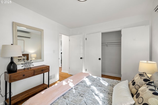 bedroom with a closet, a wall mounted air conditioner, wood finished floors, and visible vents