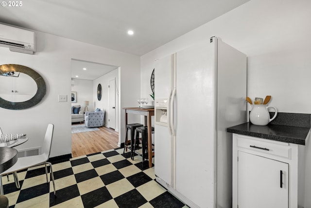 kitchen featuring light floors, a wall unit AC, white cabinetry, white fridge with ice dispenser, and dark countertops