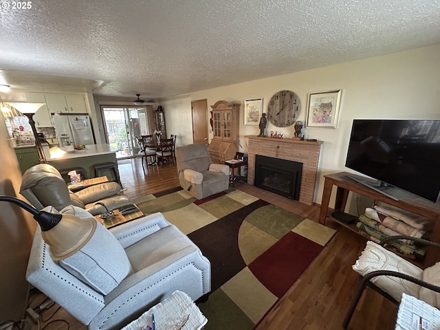 living room with ceiling fan, hardwood / wood-style floors, a brick fireplace, and a textured ceiling