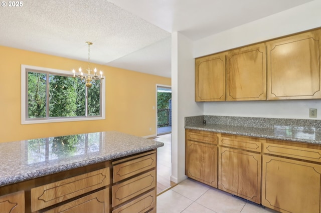 4621 SW Caldew St Unit D, Portland, OR 97219 - kitchen featuring a chandelier, light tile patterned floors, decorative light fixtures, brown cabinetry, and dark stone countertops