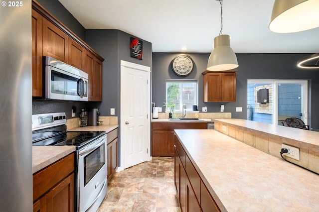 976 E 15th St, Lafayette, OR 97127 - kitchen featuring stainless steel appliances, light countertops, brown cabinets, hanging light fixtures, and stone finish flooring