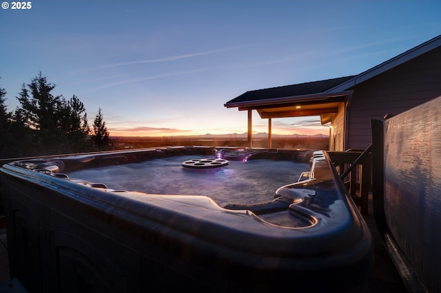 pool at dusk featuring a hot tub