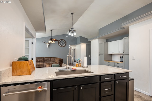 kitchen with stainless steel dishwasher, open floor plan, light stone counters, and a sink