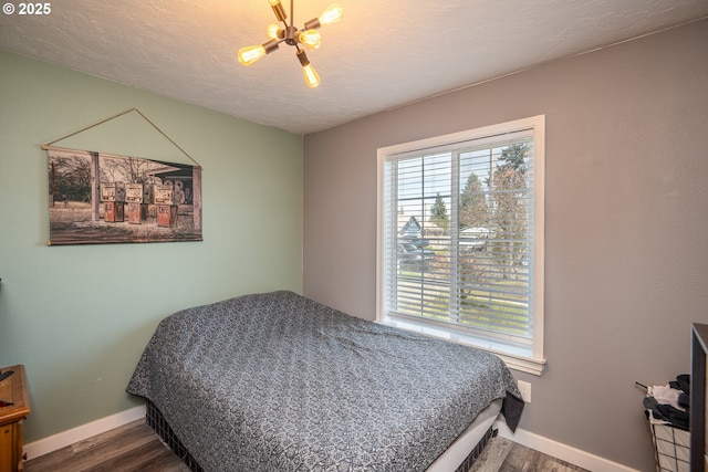bedroom featuring baseboards, a notable chandelier, wood finished floors, and a textured ceiling