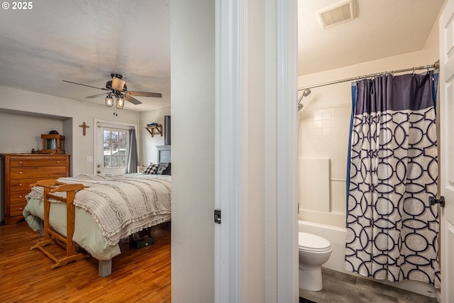 bedroom with connected bathroom, visible vents, wood finished floors, and a ceiling fan
