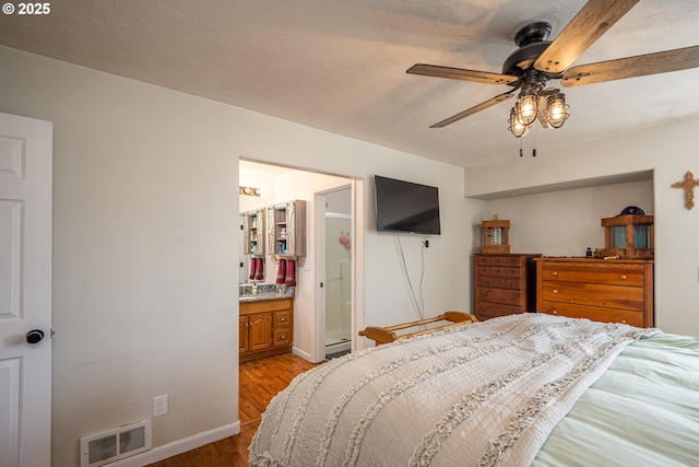 bedroom with a textured ceiling, visible vents, baseboards, wood finished floors, and baseboard heating