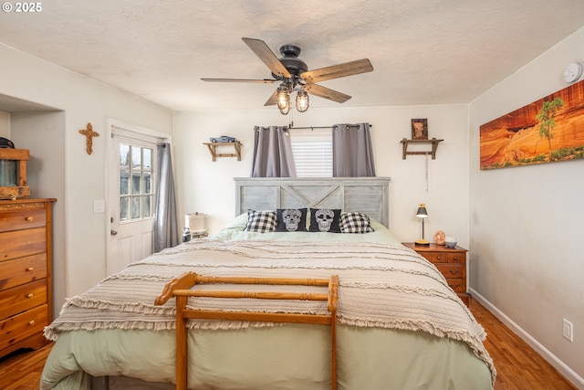 bedroom featuring a ceiling fan, a textured ceiling, multiple windows, and wood finished floors