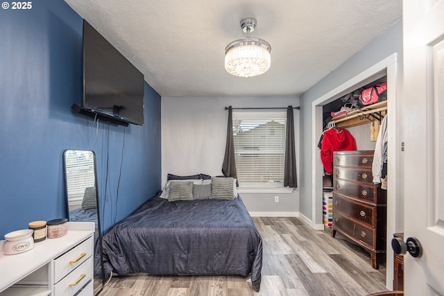 bedroom with a textured ceiling, wood finished floors, baseboards, and an inviting chandelier