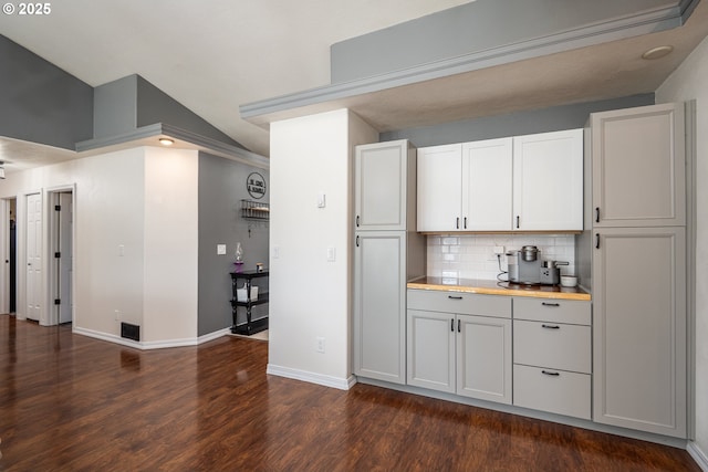 bar featuring baseboards, vaulted ceiling, tasteful backsplash, and dark wood-style flooring